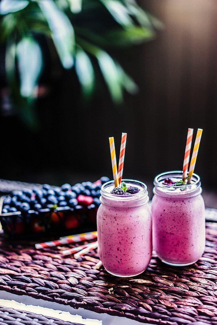 Berry smoothies in two screw-top jars with straws