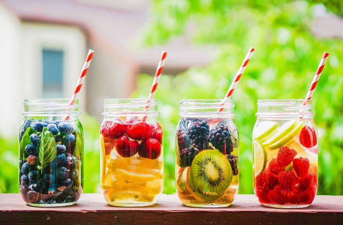 Vier fruchtige Drinks in Schraubgläsern auf Gartentisch