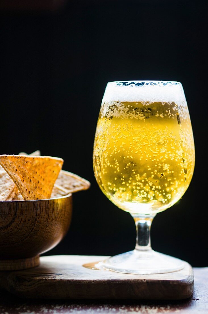A glass of lager and a bowl of tortilla crisps
