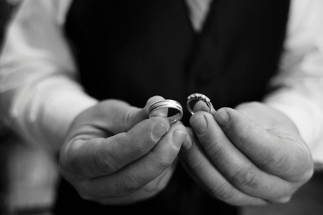Bräutigam hält Trauringe in der Hand (Ausschnitt, Schwarz-weiss-Foto)