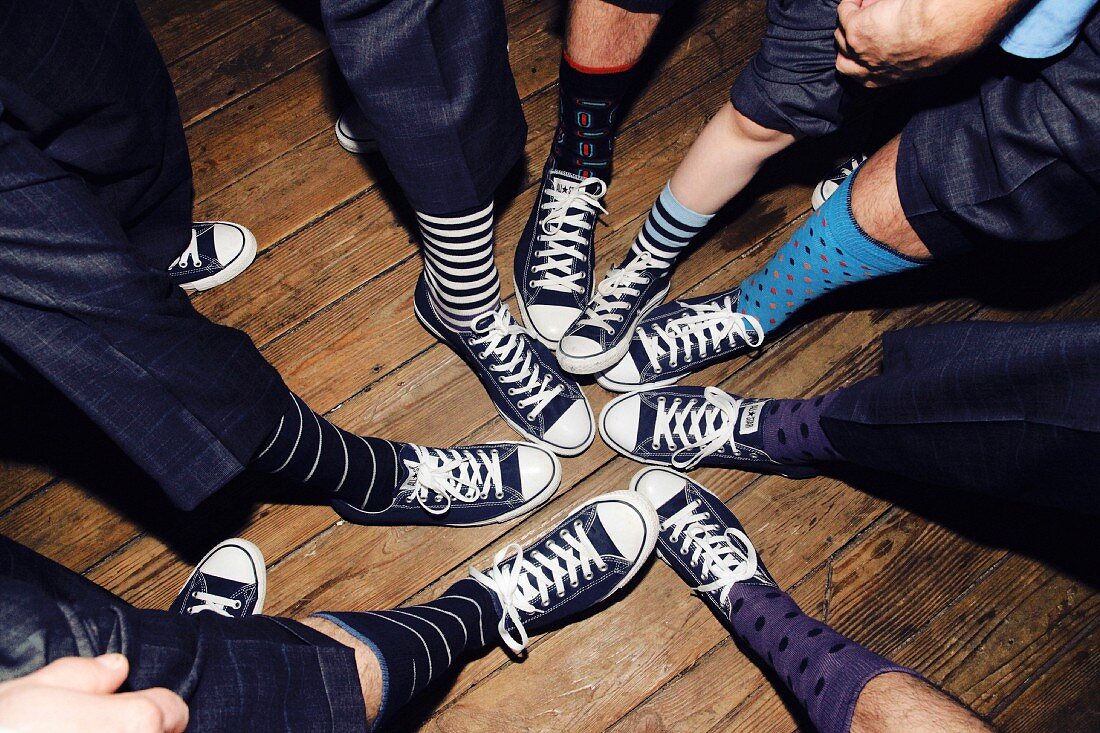 Eight men wearing the same sneakers and colourful socks with their feet together