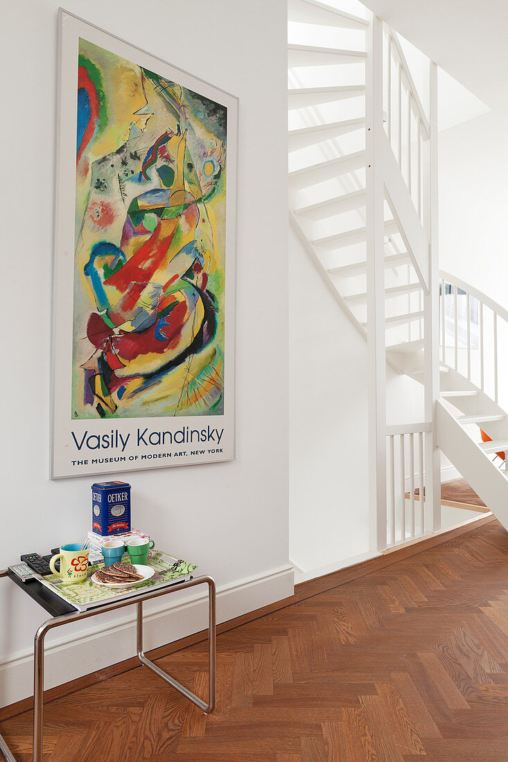 Klassiker Beistelltisch unter aufgehängtem Poster im Gang mit teilweise sichtbarer, gewendelter Treppe in Weiß