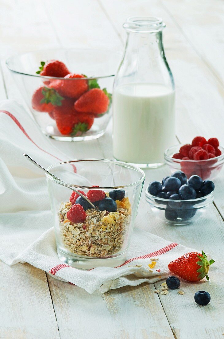 Gesundes Frühstück: Müsli mit frischen Früchten und Milch, Erdbeeren, Himbeeren, Heidelbeeren auf Holztisch