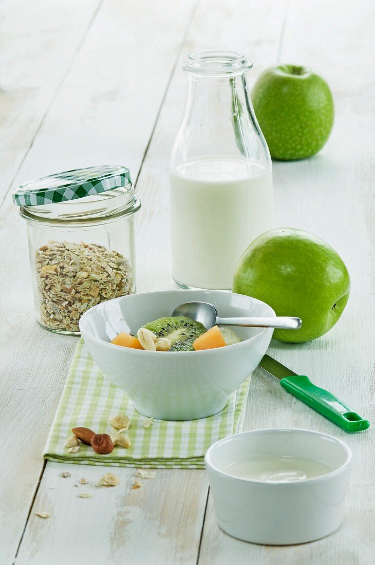 A healthy breakfast: muesli with fresh fruits, nuts and milk, kiwi, apple and melon on a wooden table