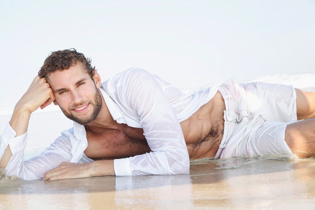 A young man wearing a white, white shirt and Bermuda shorts lying on a beach