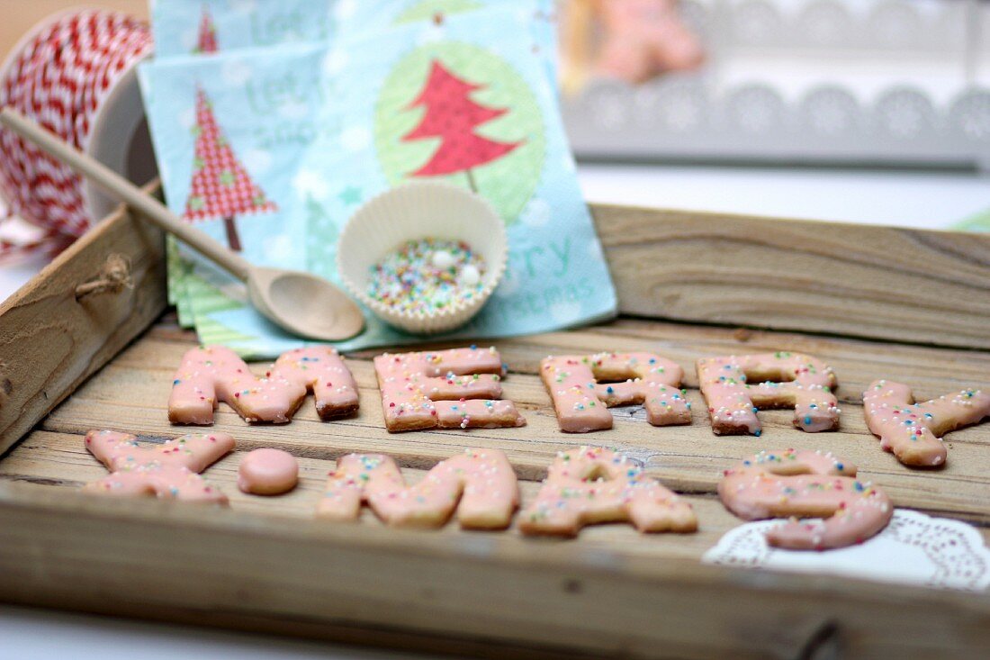 Weihnachtliche Buchstabenplätzchen mit bunten Zuckerperlen auf Holztablett