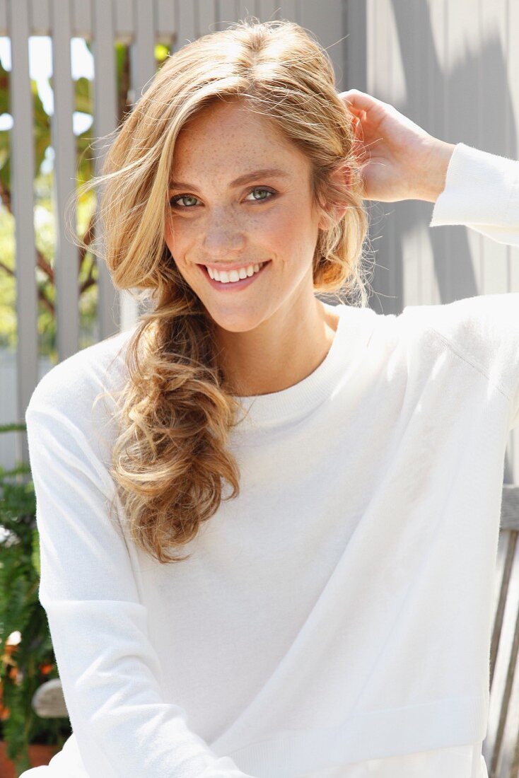 A blonde woman wearing a white top in front of a wooden wall on a terrace