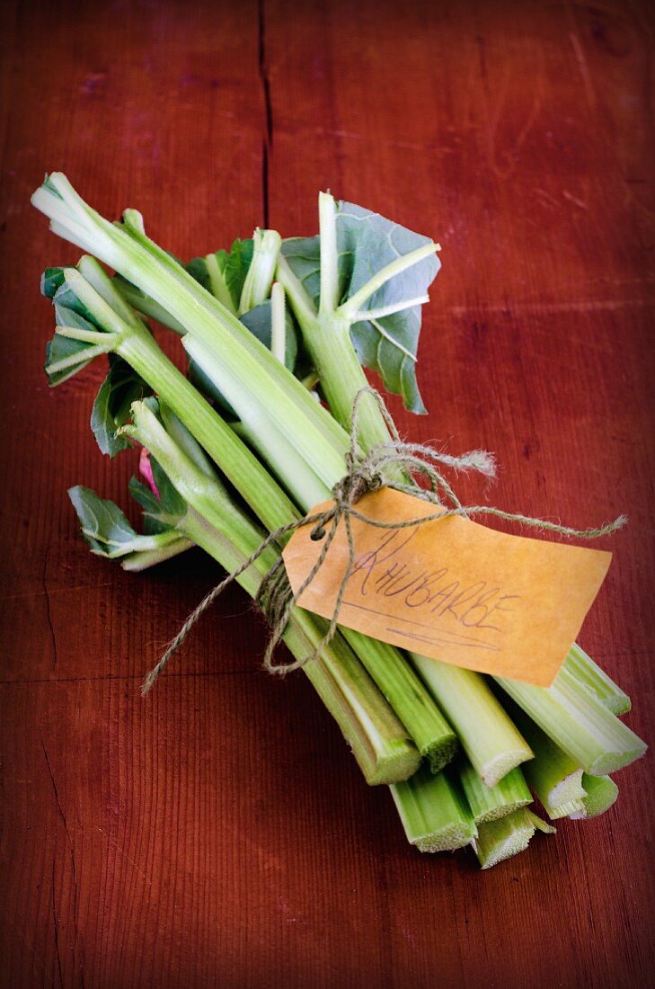 A bundle of fresh rhubarb with a paper label on a wooden board