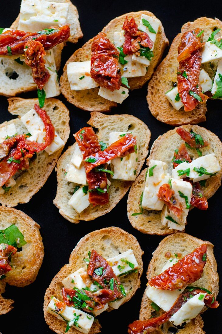 Bruschetta topped with feta cheese, dried tomatoes and herbs (seen from above)
