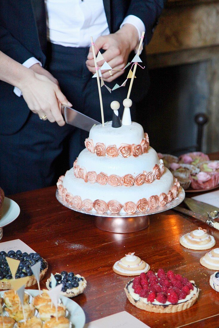 A wedding cake being cut by a bride and groom