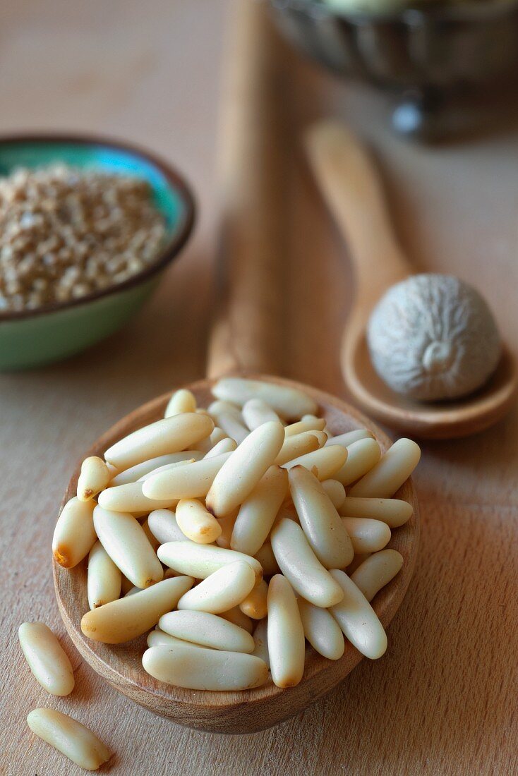 Pine nuts on a spoon with nutmeg and mustard seeds