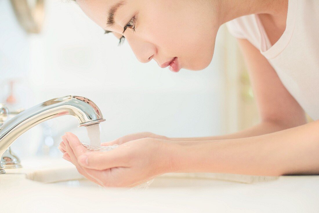 Asiatische Frau wäscht sich Gesicht am Waschbecken