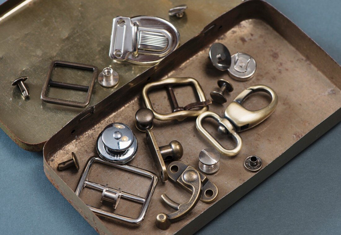 Various hooks and buckles in a metal tin