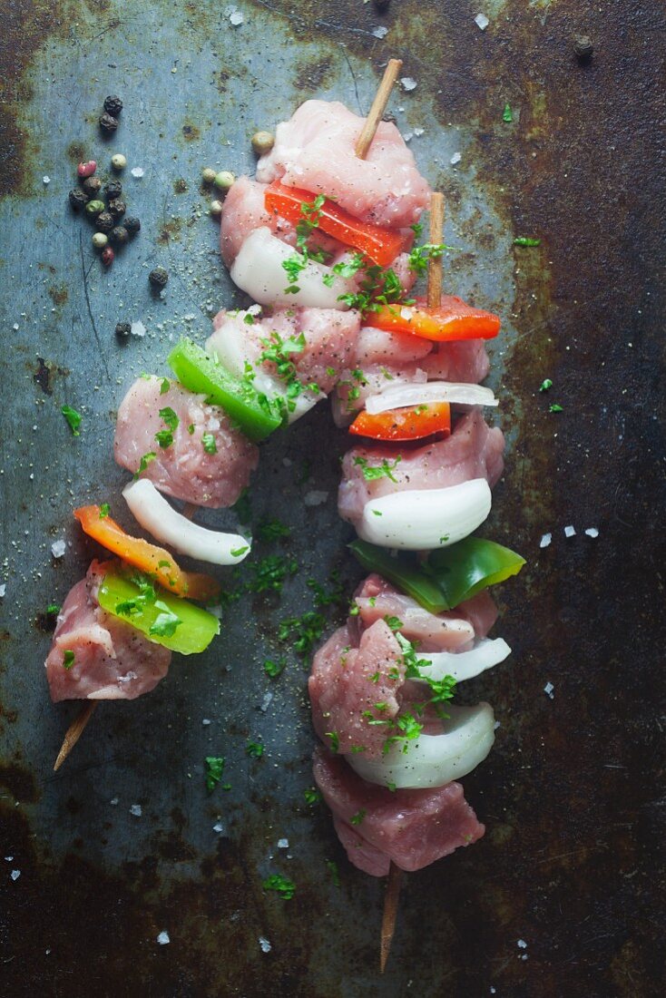 Raw pork skewers with peppers and onions on a metal surface