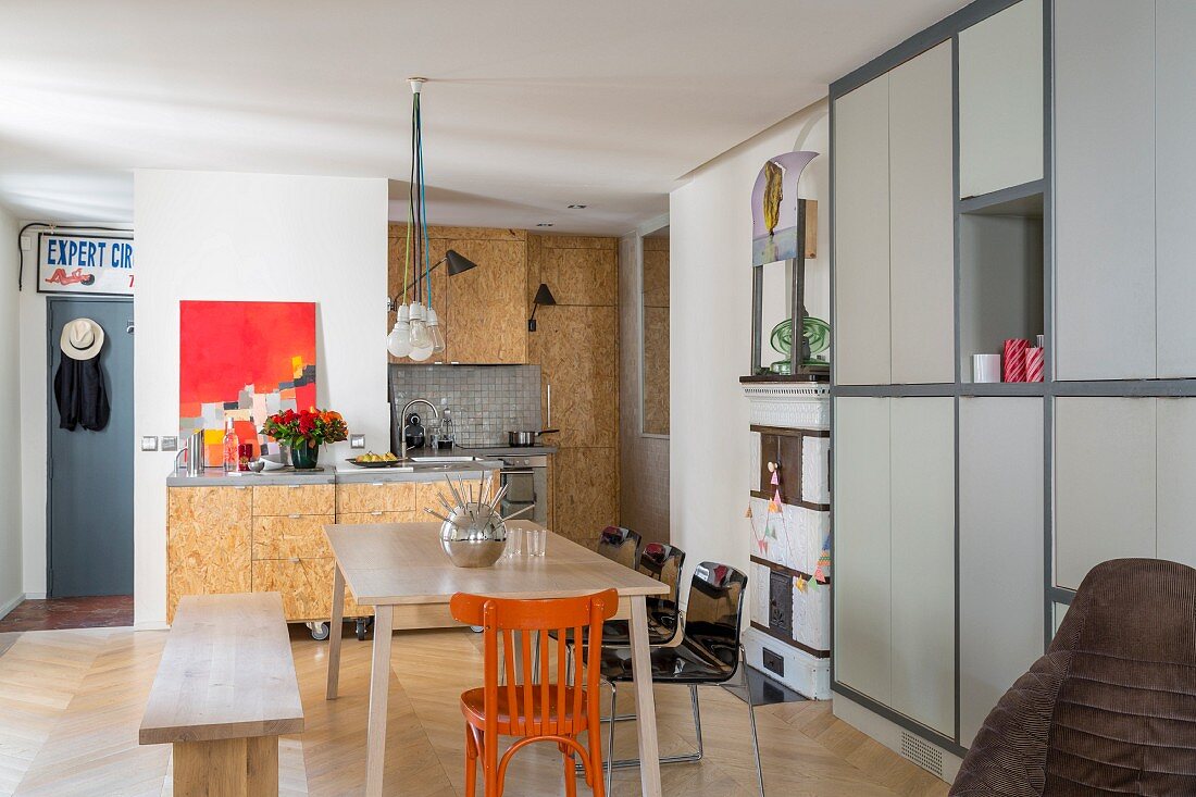 Simple wooden bench, orange chair and fitted cupboards with pale grey fronts in dining area of modern kitchen