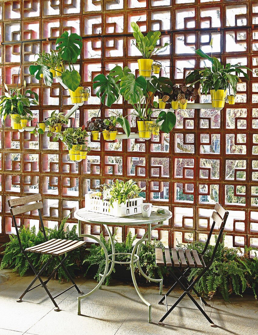 Table and two chairs on terrace next to planters hung on decorative perforated screen