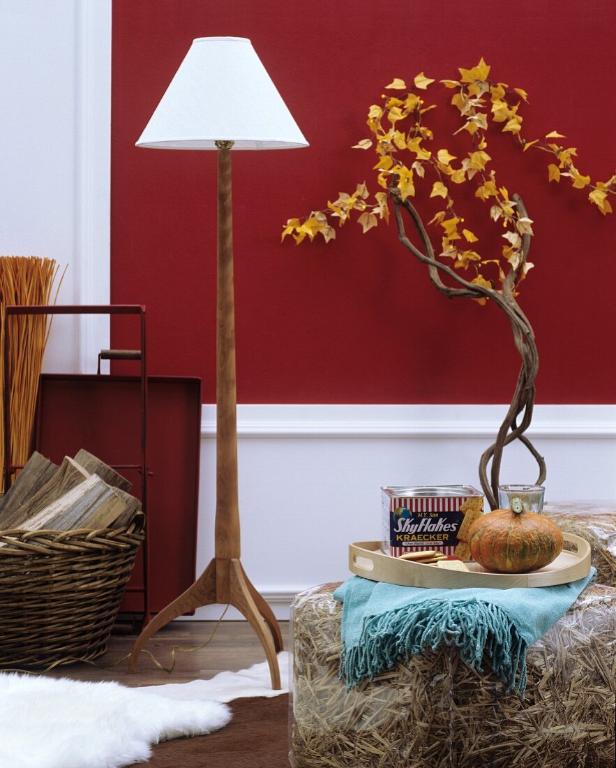Herbstliche Wohnaccessoires: Stehleuchte mit Holzfuss, strohgefüllte Plastikhocker und Äste dekoriert mit Blättergirlande
