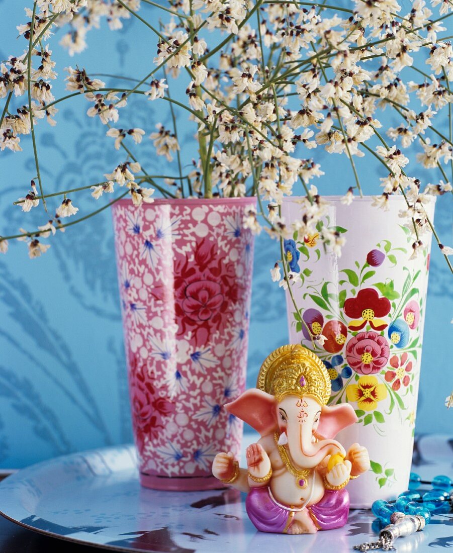 Zwei Porzellanvasen mit dekorativen Blütenmustern davor Ganesha-Figur auf Tablett