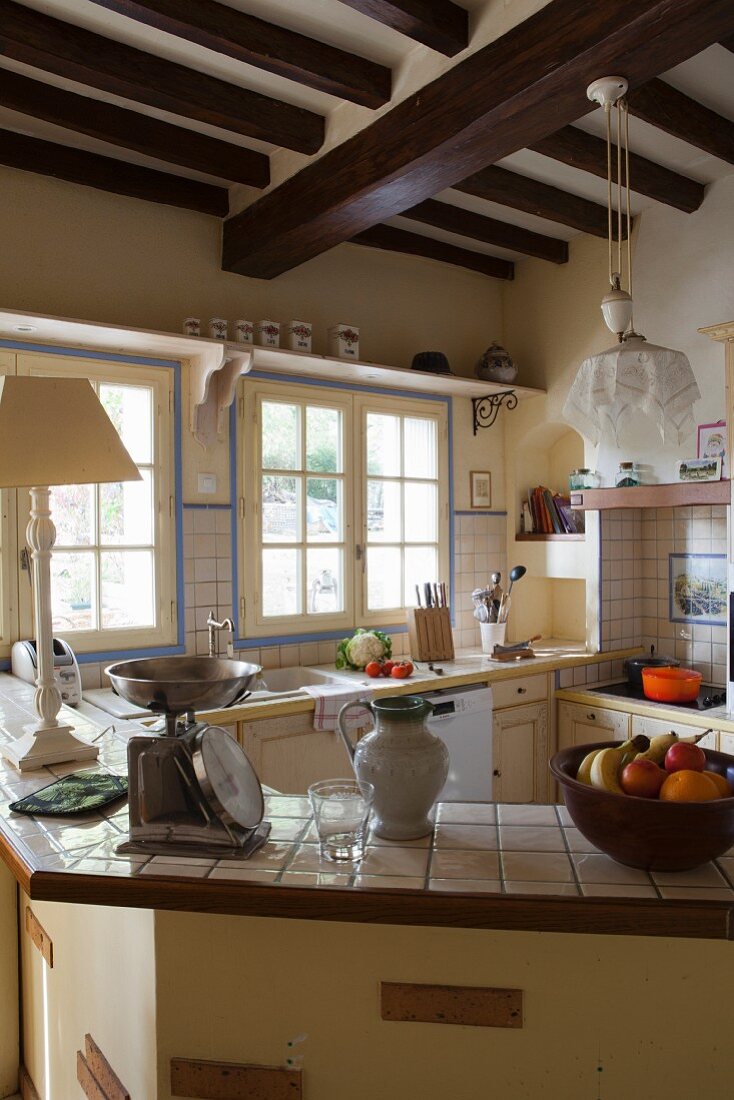 Abgewinkelte Theke mit gefliester Oberfläche in Landhausküche mit Holzbalkendecke