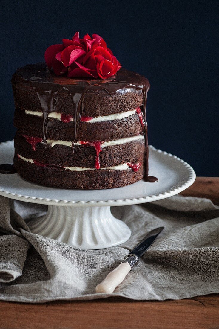 A chocolate cake with raspberry jam, chocolate glaze and rose petals