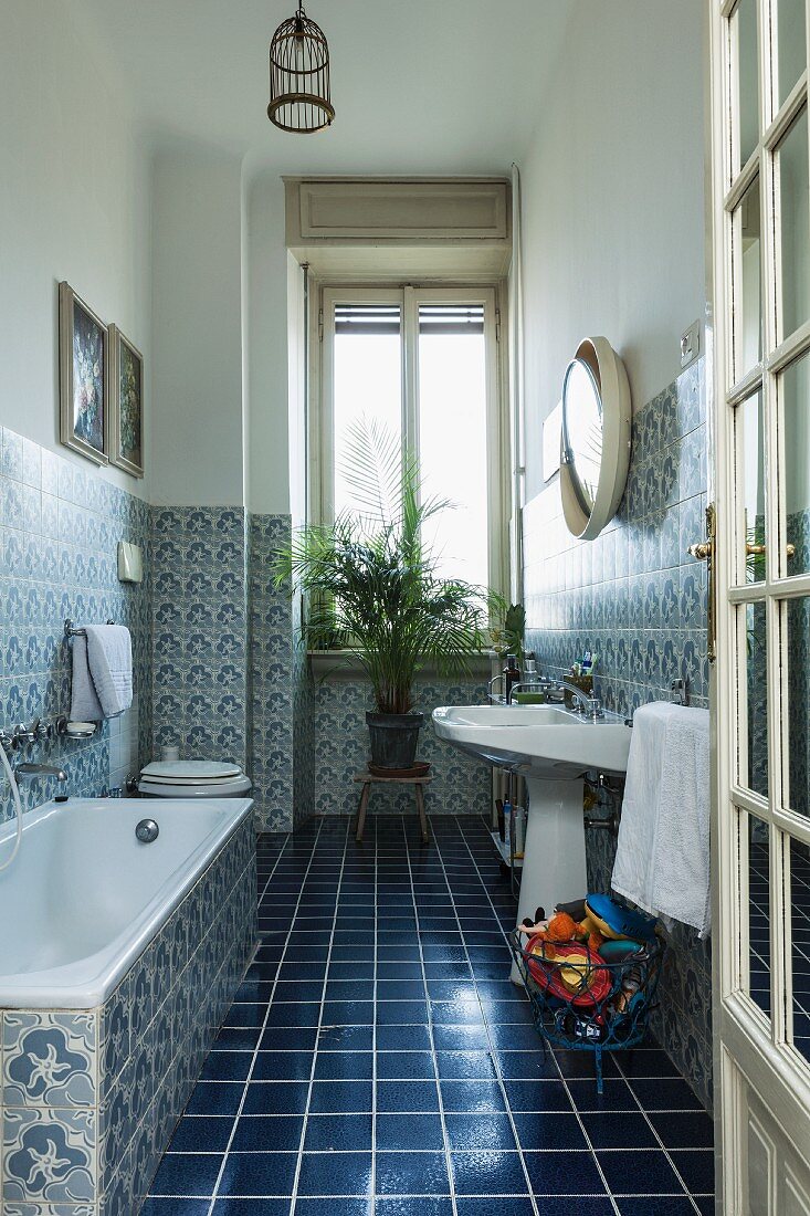 Bathroom with dark blue floor tiles, patterned wall tiles and potted palm on stool below window