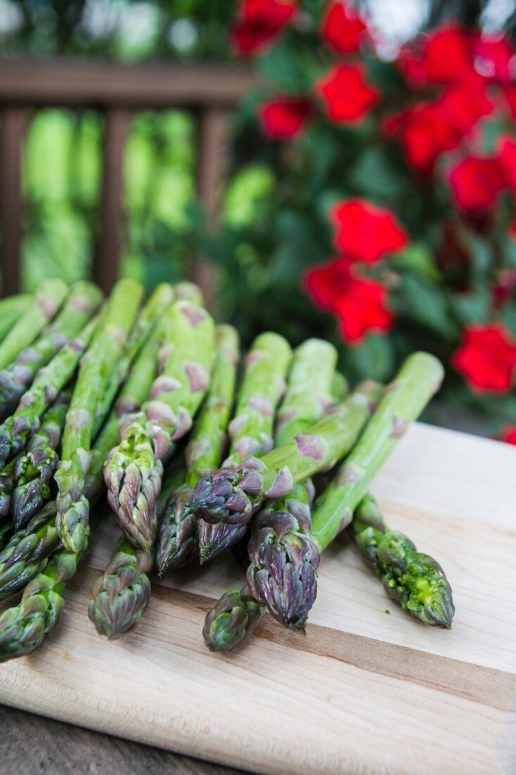 Green asparagus on a chopping board with red flowers in the background