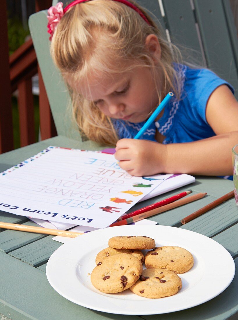 Kleines Schulmädchen mit Schulheft und Cookies