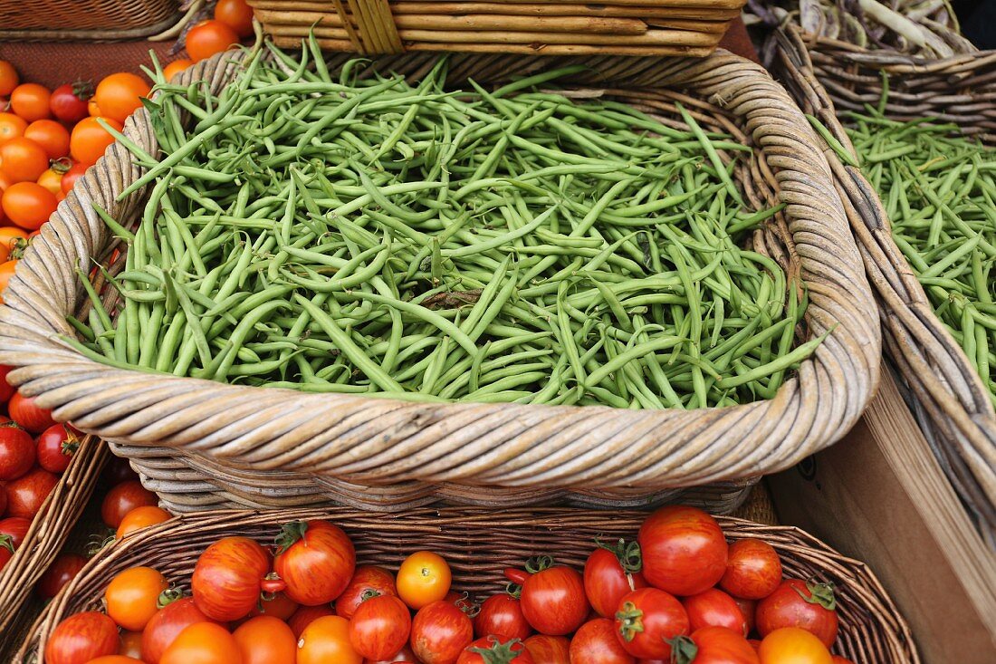 Grüne Bohnen und Tomaten in geflochtenen Körben auf dem Markt