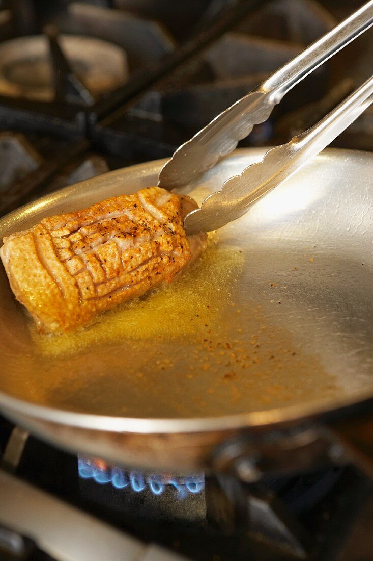 Duck breast being fried in a pan on a gas stove