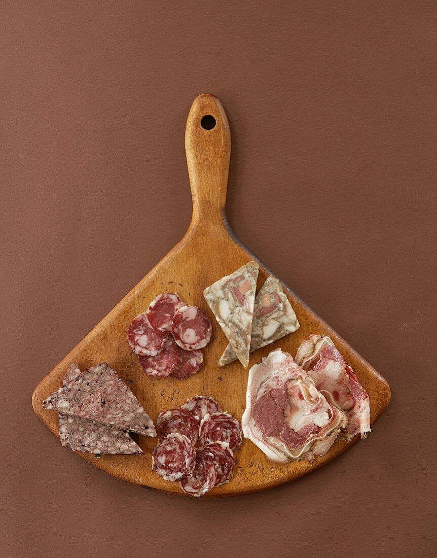 Slices of various Italian meats on a wooden board (seen from above)