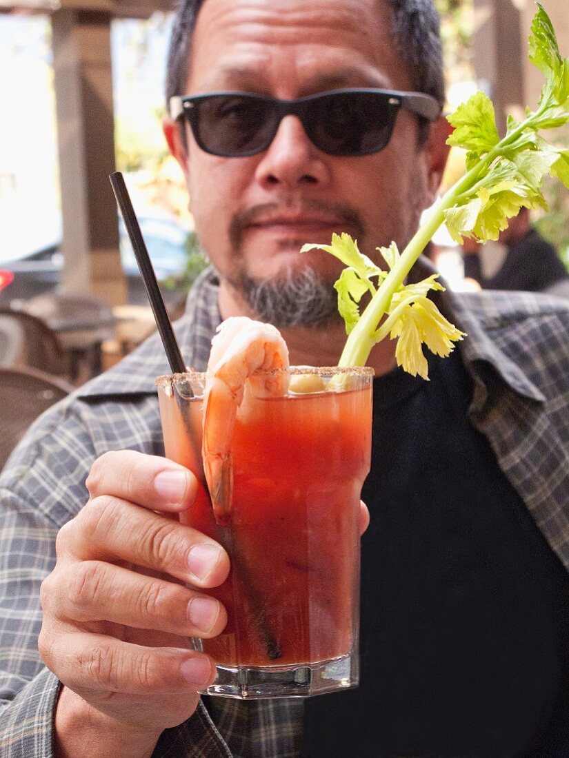 Mann mit Bart & Sonnenbrille hält Glas mit Bloody Mary in der Hand