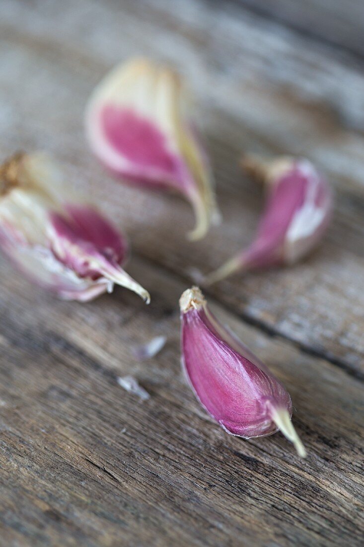 Four garlic cloves on a wooden surface (close up)