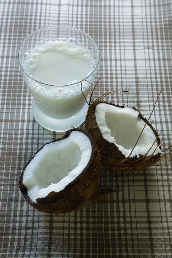 A glass of coconut milk and a halved coconut