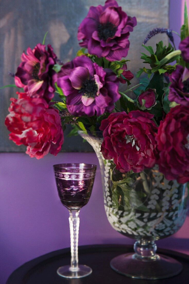 Violettes Kristall Likörglas neben Blumenstrauss in verschiedenen Rottönen