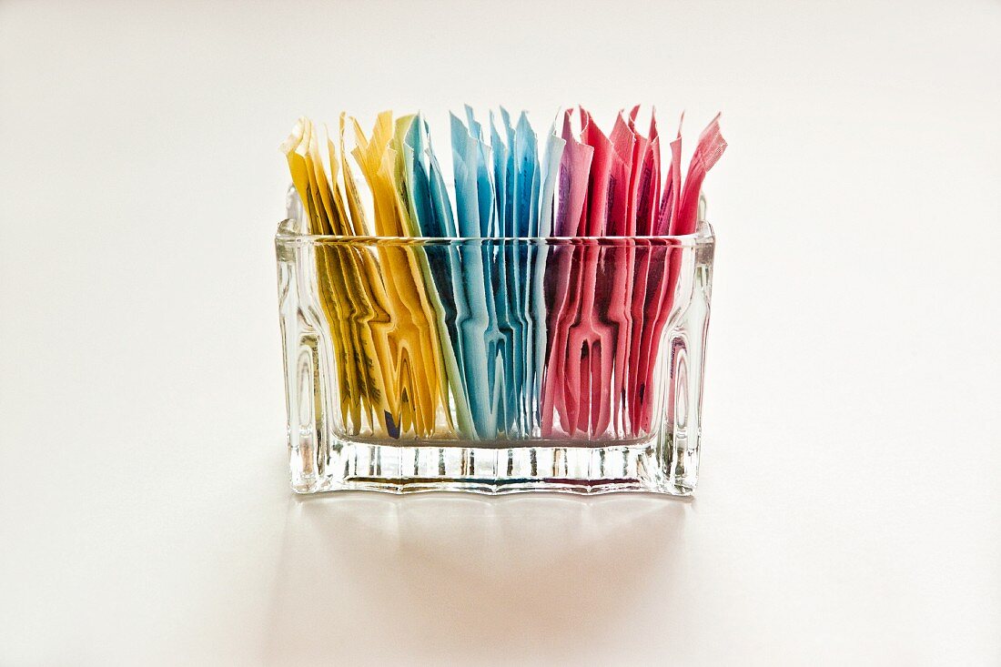 Colourful sachets of sweeteners in a glass container