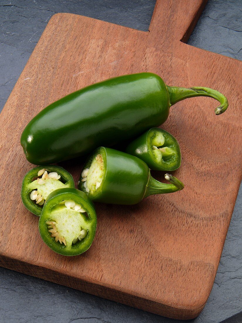 Two jalapeños, one sliced, on a chopping board