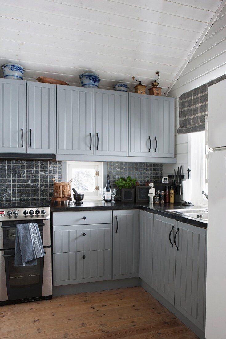 Ländliche Einbauküche mit hellgrau lackierten Schränken, vor holzverschalten Wänden in Weiß