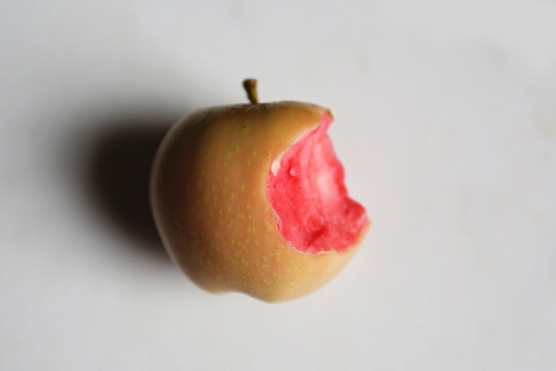 A pink pearl apple with a bite taken out of it on a marble surface