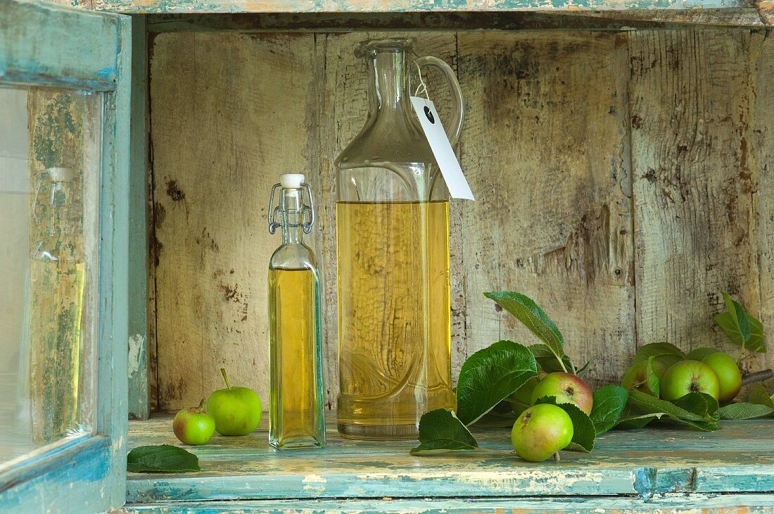 Two bottles of apple vinegar with paper labels and apples in a rustic cupboard niche