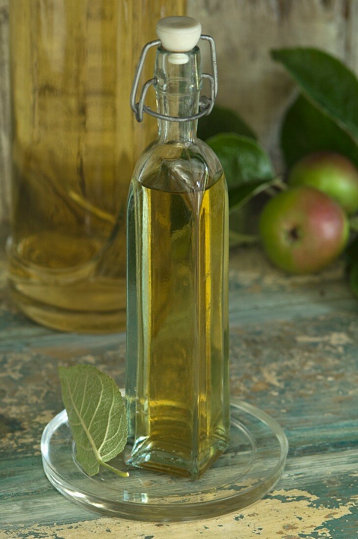 A bottle of apple vinegar and apples in a rustic cupboard niche