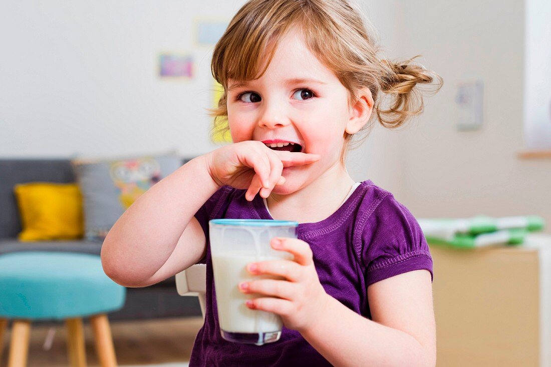 A little girl with pigtails holding a glass of milk