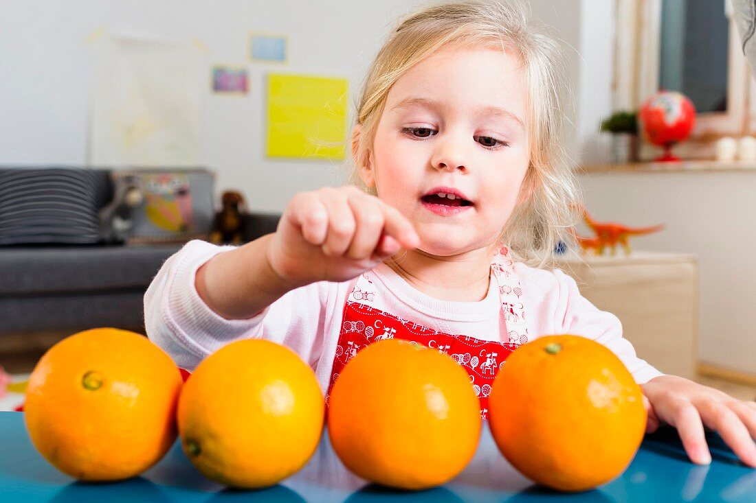 A little girl sitting at a table counting oranges