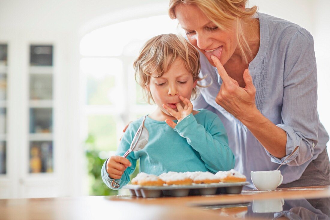 Mutter und Sohn bestäuben Muffins mit Puderzucker & naschen dabei