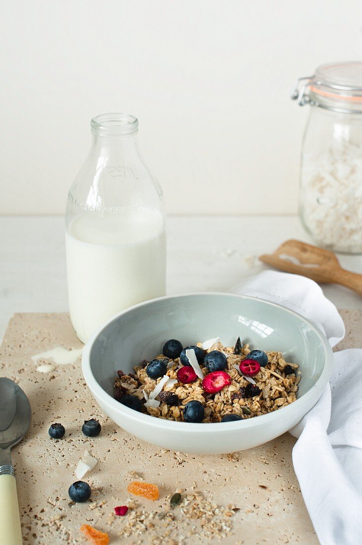 A bowl of muesli with fresh berries and a bottle of milk