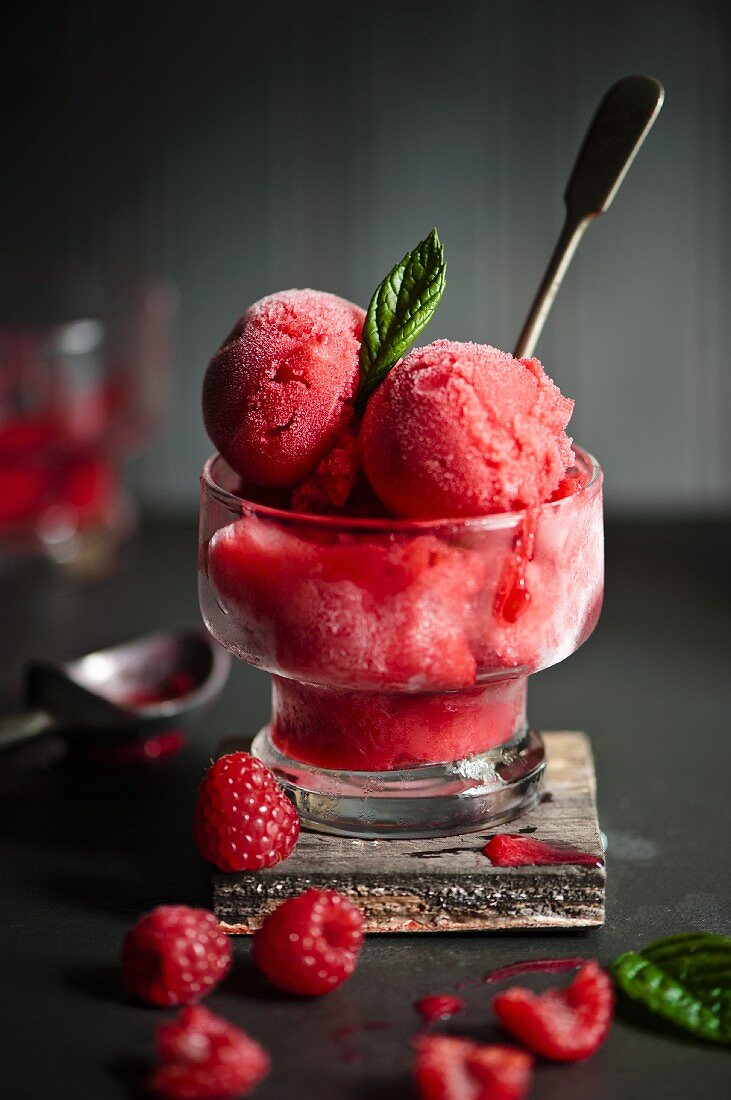 A glass of raspberry sorbet with a spoon and fresh raspberries