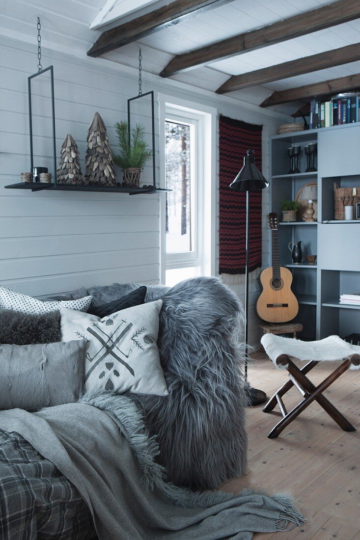 Scatter cushions and animal-skin blanket on sofa in wood-clad cabin interior