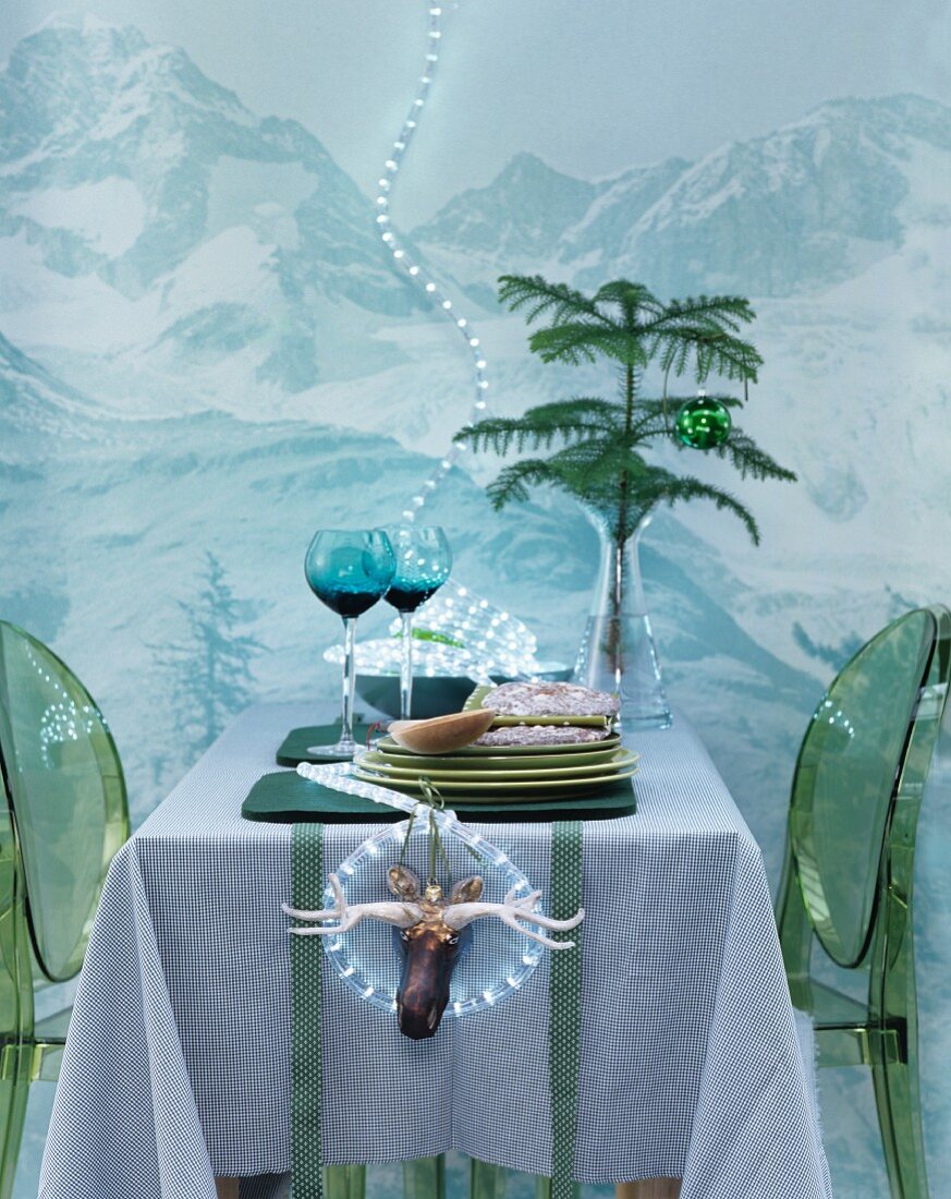 Esstisch mit grünen Plexiglasstühlen vor Wand mit Bergmotiv & Lichterkette