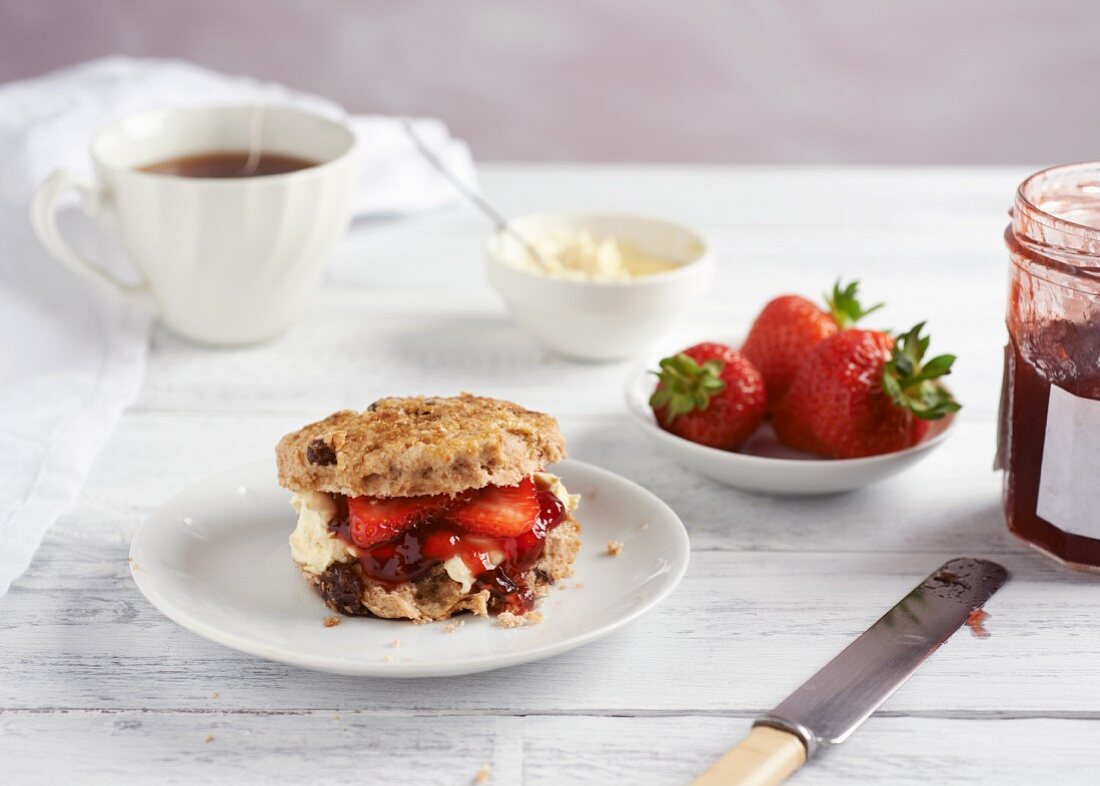 A scone with clotted cream, strawberries and jam served with tea