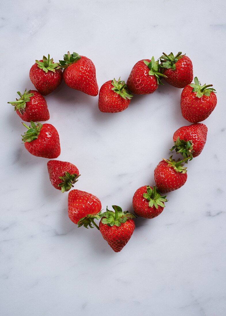 A heart of fresh strawberries on a white surface