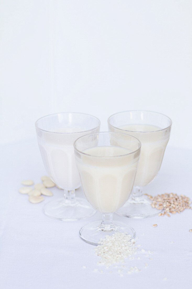 Rice milk, almond milk and nut milk in glass on white wooden surface